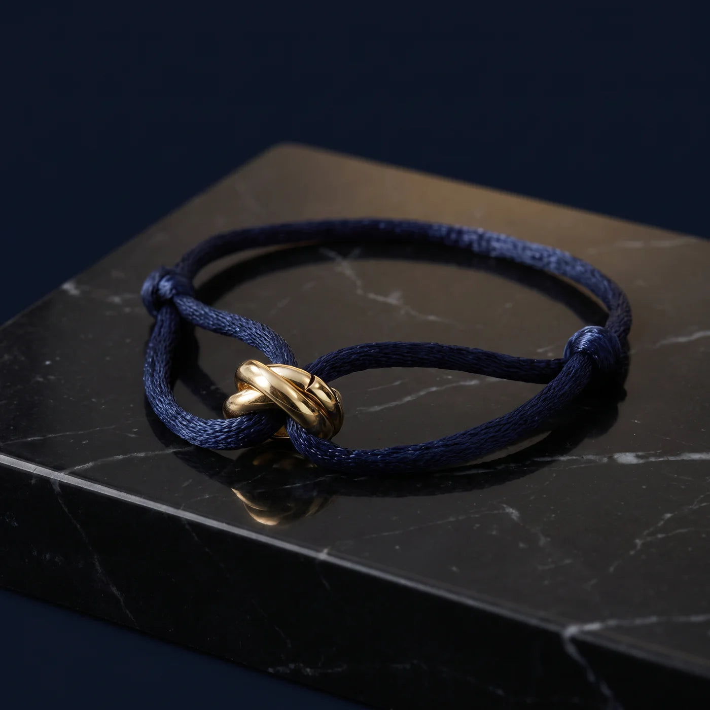 Bracelet Trinité — marineblaue Kordel mit goldenem Trinity-Ring auf Mitternachts-Bühne